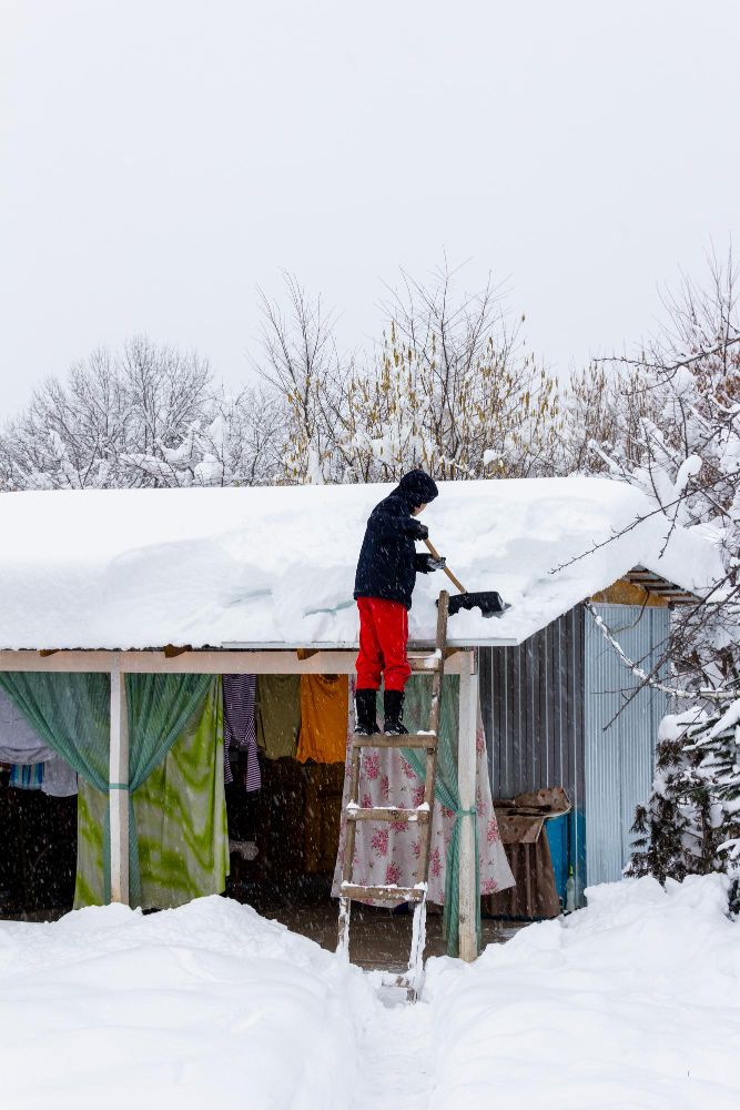 A person using a roof rake to remove snow from a pole barn roof