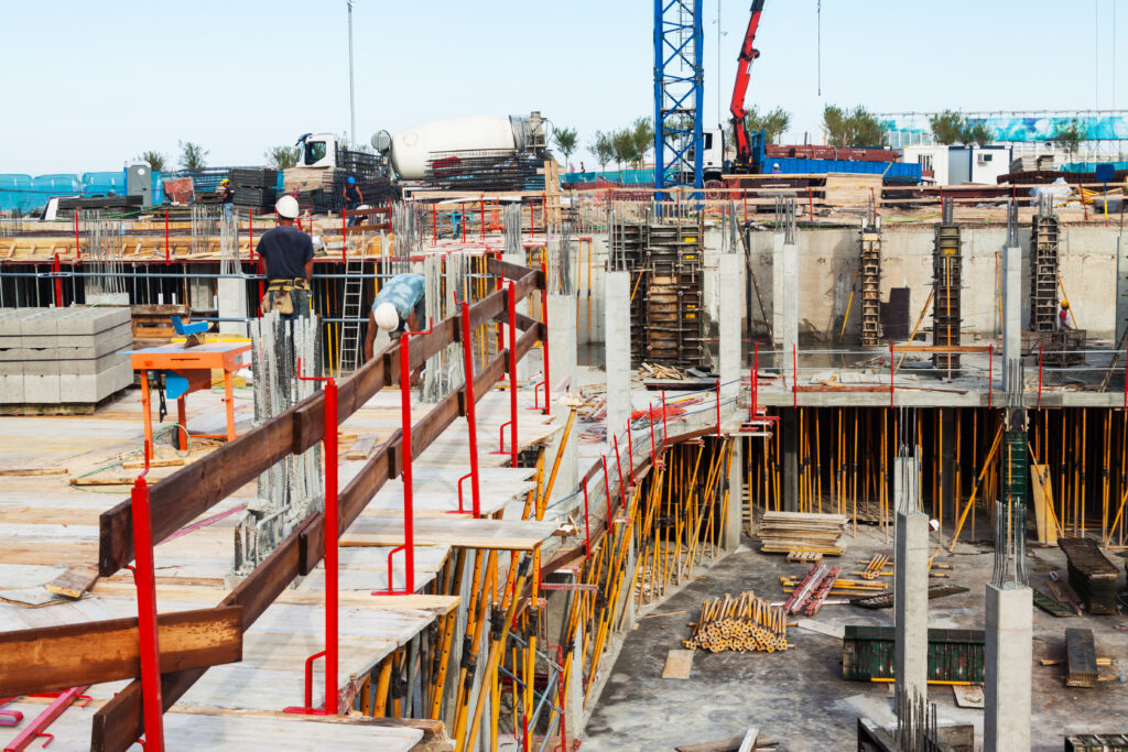 Construction site with workers assembling a multi-story steel building structure.